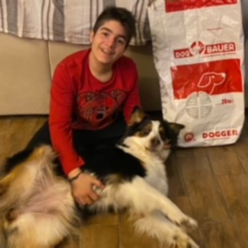 Ragazza felice fa le coccole al suo Australian Shepherd, sullo sfondo il sacco delle crocchette Dogbauer: scoprile anche tu!