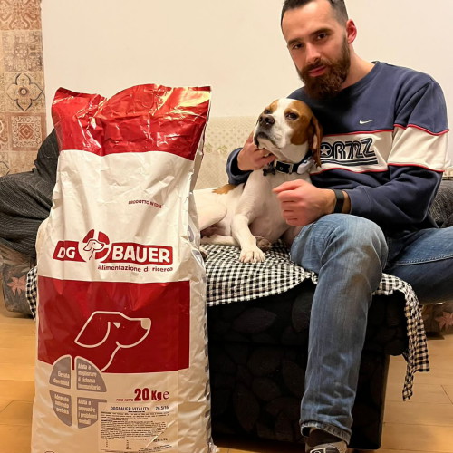 Uomo seduto sul divano con il suo cane Pointer e davanti il sacco di crocchette Dogbauer