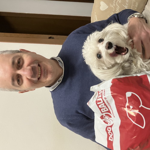 Uomo sorridente con in braccio il suo cane maltese e il sacco delle crocchette Dogbauer